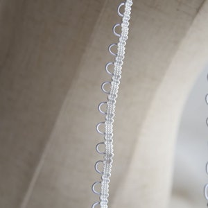 May include: White elastic trim with small loops along the edge. The trim is commonly used for sewing projects.