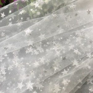 May include: White tulle fabric with silver glitter stars. The fabric is sheer and delicate, perfect for crafting or decorating.