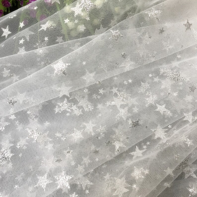 May include: White tulle fabric with silver glitter stars. The fabric is sheer and delicate, perfect for crafting or decorating.