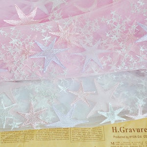 May include: Pink and white tulle fabric with embroidered stars. The fabric is layered, with the top layer being pink and the bottom layer being white. The stars are silver and pink.