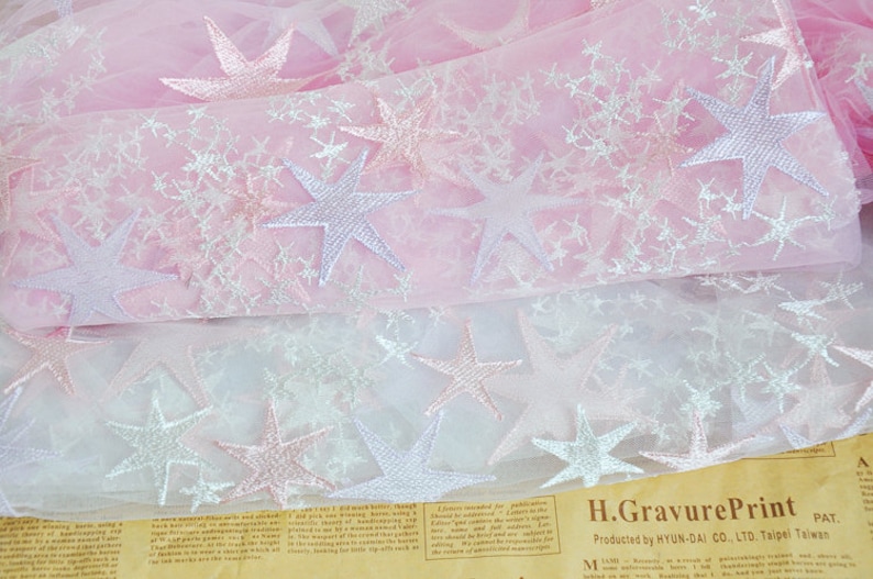 May include: Pink and white tulle fabric with embroidered stars. The fabric is layered, with the top layer being pink and the bottom layer being white. The stars are silver and pink.