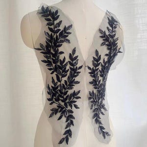 Peut inclure: Applique florale noire à perles sur un tissu de maille transparent. L'applique présente un motif délicat de feuilles et de branches.