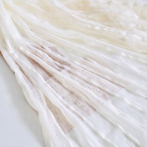 May include: White sheer fabric with a textured, dotted pattern. The fabric is pleated and has a soft, delicate look.