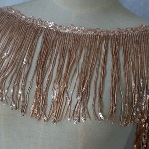 May include: A gold sequined fringe trim with a delicate, shimmering texture. The fringe is approximately 2 inches long and is perfect for adding a touch of glamour to any project.