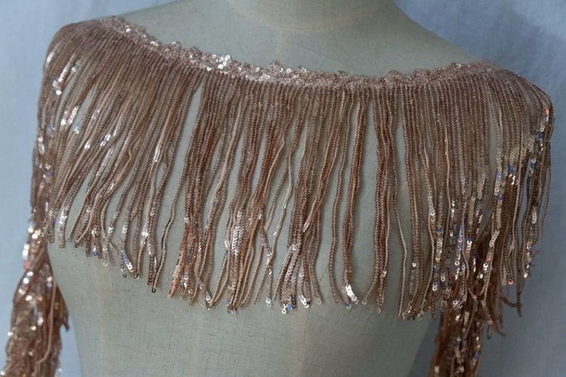 May include: A gold sequined fringe trim with a delicate, shimmering texture. The fringe is approximately 2 inches long and is perfect for adding a touch of glamour to any project.