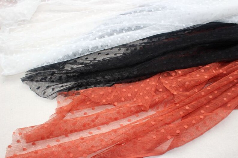 May include: Three pieces of dotted mesh fabric in white, black, and orange. The fabric is soft and sheer, with a delicate polka dot pattern.