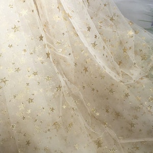 May include: White tulle fabric with a gold glitter star pattern. The fabric is sheer and has a delicate texture.