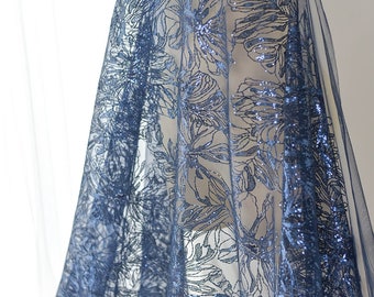 May include: Blue floral lace fabric with glitter accents. The fabric has a delicate, sheer texture and is perfect for creating elegant garments or accessories.