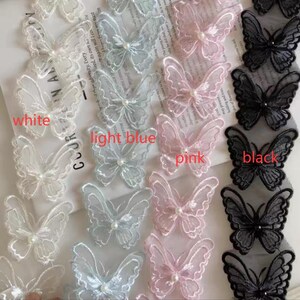 Könnte beinhalten: Nahaufnahme von Schmetterlingsapplikationen in Weiß, Hellblau, Rosa und Schwarz. Jeder Schmetterling hat eine perlenartige Mitte. Das Bild enthält die Wörter "white", "light blue", "pink" und "black".