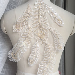 May include: White lace applique with gold sequins in a feather design. The applique is perfect for adding a touch of elegance to any garment.