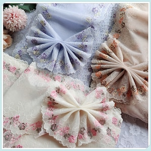 May include: Three pieces of delicate lace fabric with floral embroidery. The fabric is in shades of white, light blue, and light pink. The fabric is arranged in a fan shape, creating a decorative and elegant design.