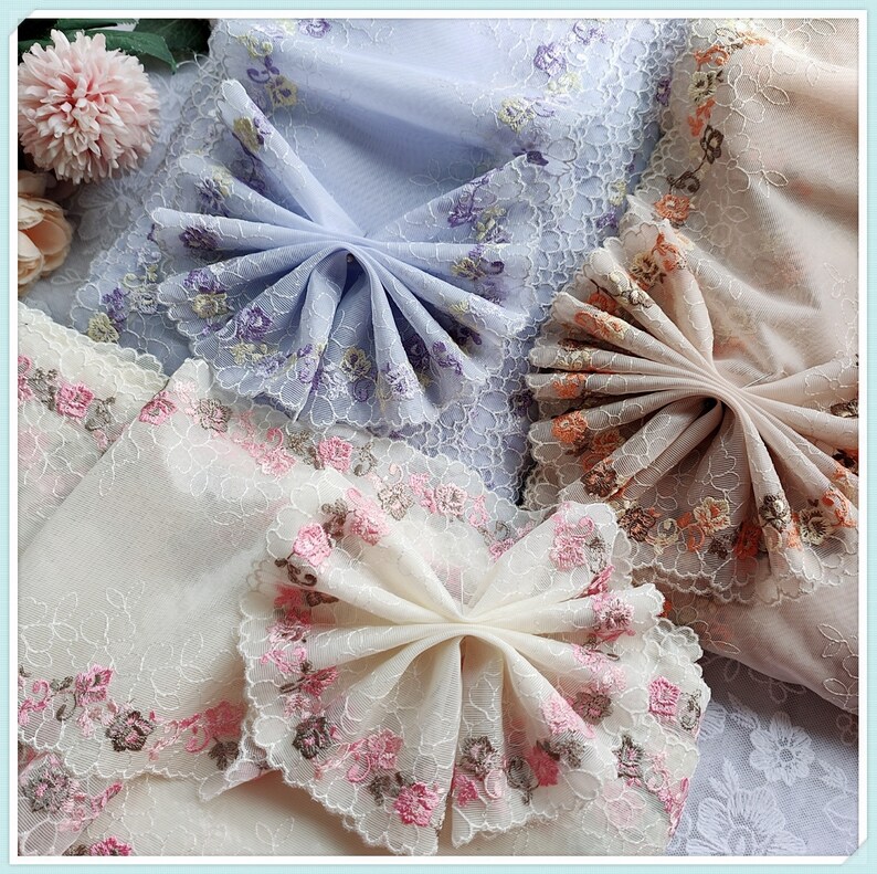 May include: Three pieces of delicate lace fabric with floral embroidery. The fabric is in shades of white, light blue, and light pink. The fabric is arranged in a fan shape, creating a decorative and elegant design.