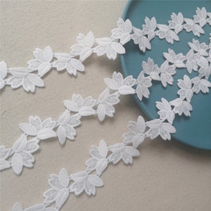 May include: White lace trim with a delicate floral design. The trim features small, intricate flowers and leaves, creating a delicate and feminine look.