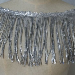 May include: Silver sequined fringe trim with a scalloped edge. The fringe is about 2 inches long.