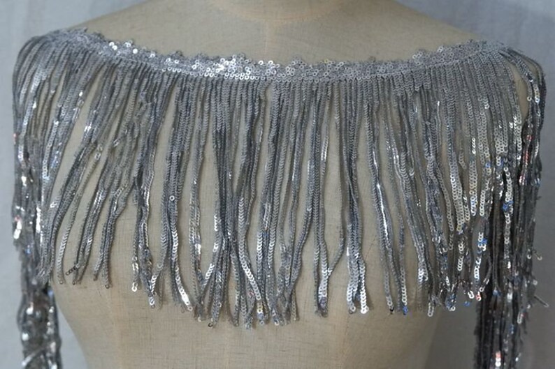 May include: Silver sequined fringe trim with a scalloped edge. The fringe is about 2 inches long.