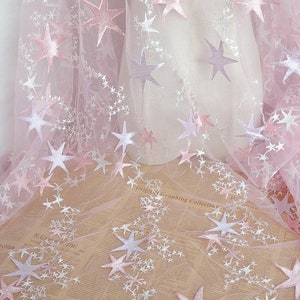 May include: Pink tulle fabric with white and pink embroidered stars. The fabric is sheer and delicate, and the stars are scattered randomly across the surface.