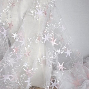 May include: White tulle fabric with pink embroidered stars. The fabric is sheer and delicate, perfect for crafting or adding a touch of sparkle to any project.