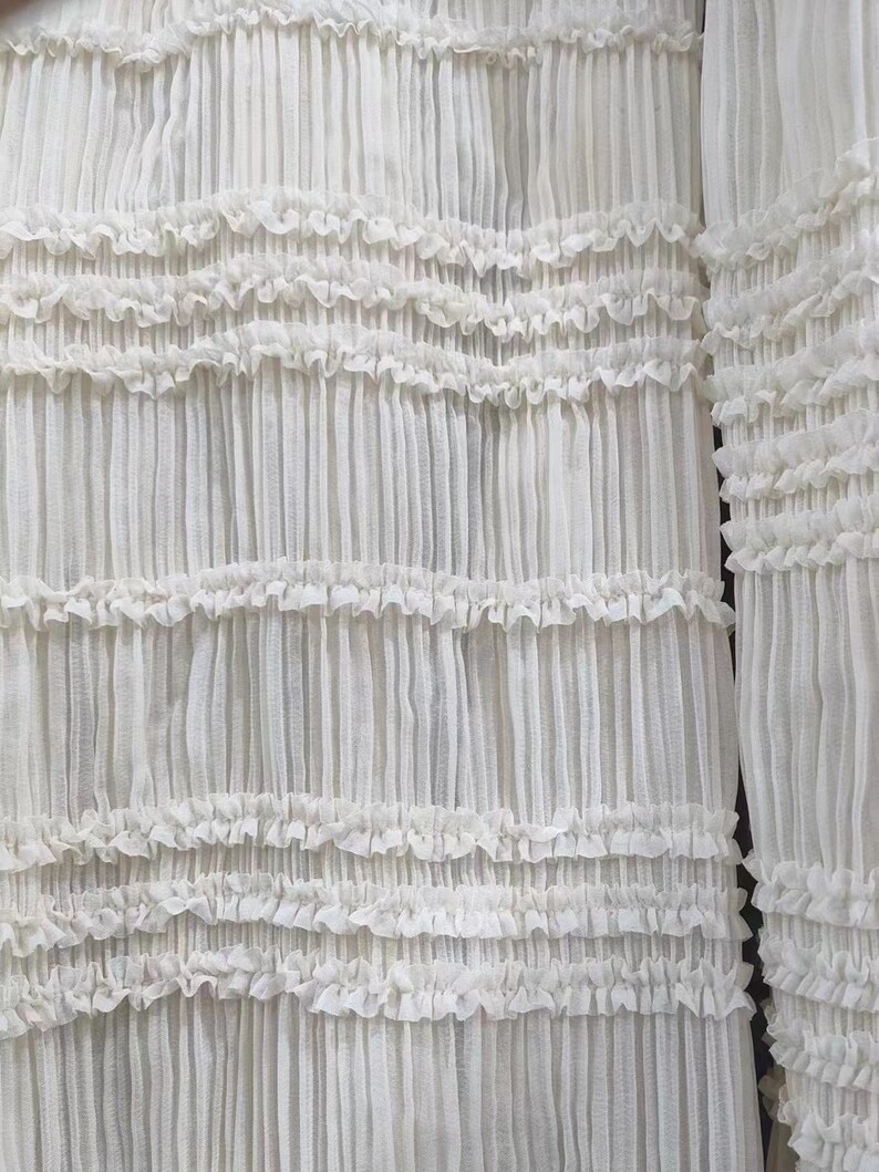 May include: White sheer fabric with a ruffled texture. The fabric is pleated and has a delicate, airy feel.