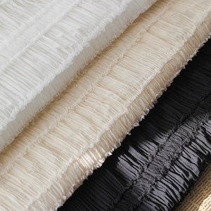 May include: Three layers of white, cream, and black ruffled fabric. The fabric is soft and delicate, with a slightly textured surface.