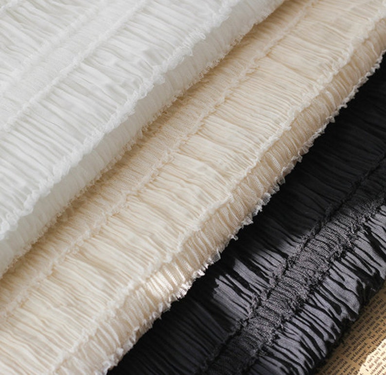 May include: Three layers of white, cream, and black ruffled fabric. The fabric is soft and delicate, with a slightly textured surface.