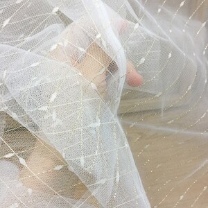 May include: White tulle fabric with gold glitter thread woven throughout. The fabric is sheer and delicate.