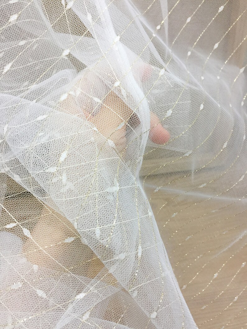 May include: White tulle fabric with gold glitter thread woven throughout. The fabric is sheer and delicate.