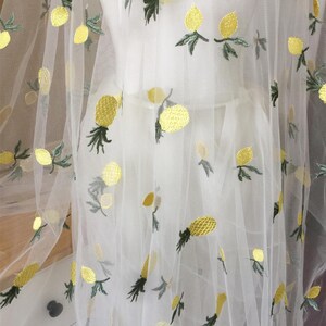 Puede incluir: Tela blanca transparente con diseños de piña bordados en amarillo y verde.
