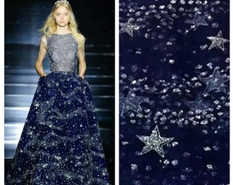 May include: A navy blue tulle fabric with silver glitter and star-shaped sequins. The fabric is perfect for creating a glamorous and festive look.