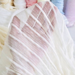 May include: White sheer fabric with a dotted pattern and vertical stripes. The fabric is soft and delicate, perfect for crafting and sewing projects.