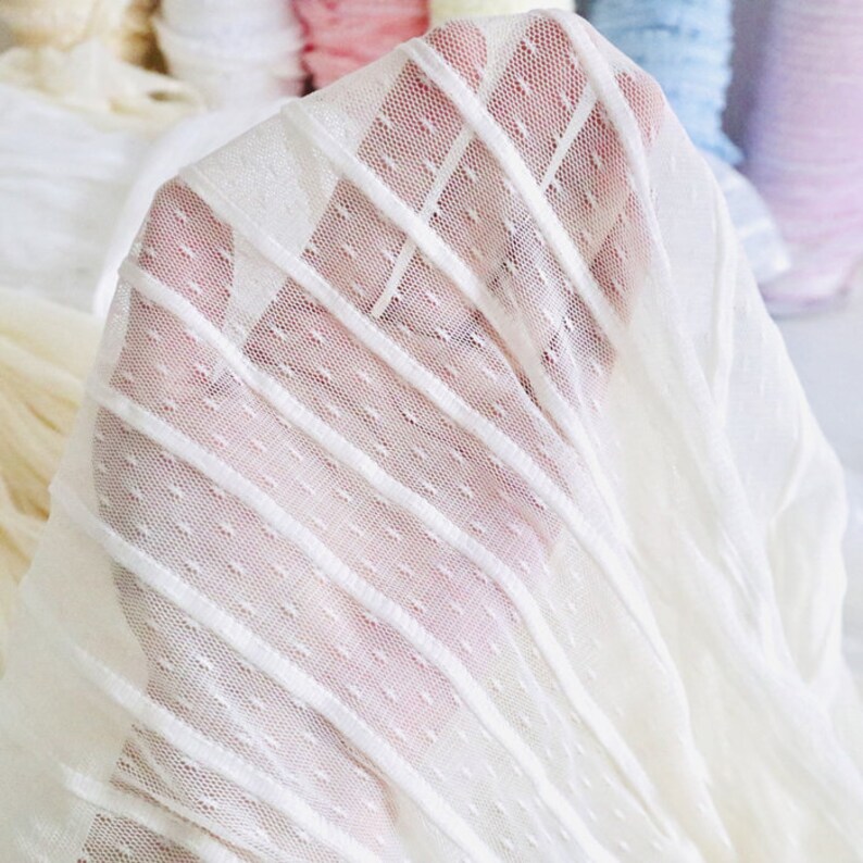 May include: White sheer fabric with a dotted pattern and vertical stripes. The fabric is soft and delicate, perfect for crafting and sewing projects.