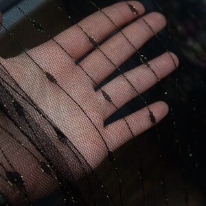 May include: Black sheer fabric with gold thread woven throughout. The fabric is delicate and has a soft, flowing texture.
