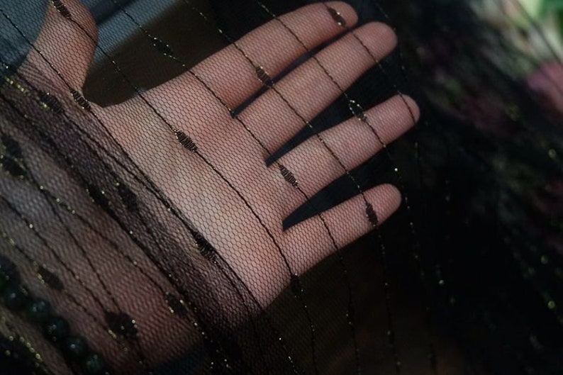 May include: Black sheer fabric with gold thread woven throughout. The fabric is delicate and has a soft, flowing texture.