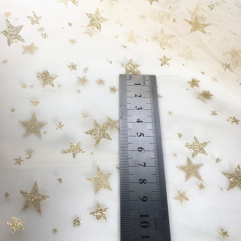 May include: White tulle fabric with gold glitter stars. A ruler is placed on the fabric to show the scale. The ruler measures 10.5 cm.