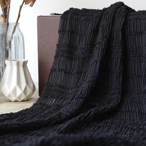 May include: Black fabric with a crinkled texture. The fabric is folded and draped over a wooden box.