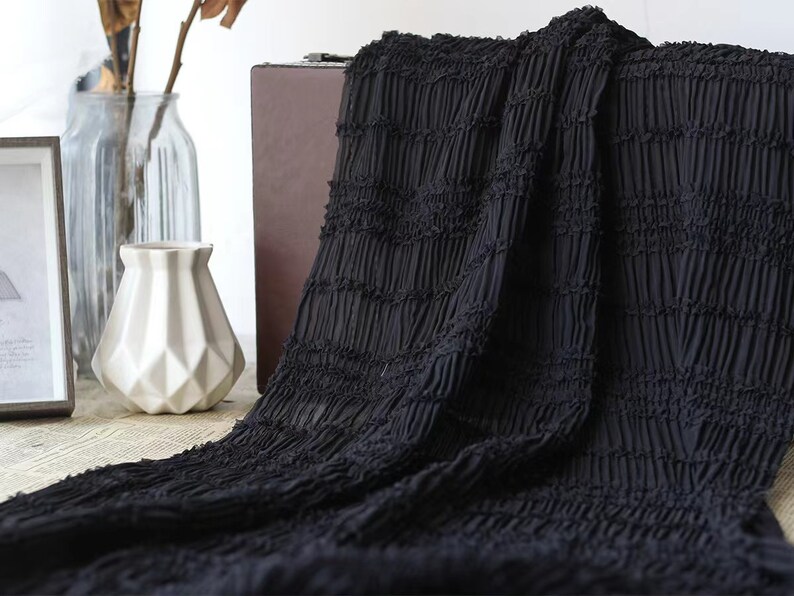 May include: Black fabric with a crinkled texture. The fabric is folded and draped over a wooden box.
