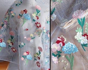 Puede incluir: Tela blanca transparente con diseños florales bordados en tonos de rosa, rojo, azul, verde y amarillo. La tela tiene una textura delicada y aireada, perfecta para manualidades o para agregar un toque de elegancia a cualquier proyecto.