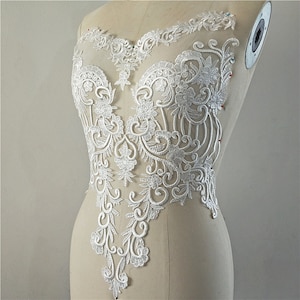 May include: White lace applique with a floral design. The lace is delicate and intricate, with a variety of floral motifs. The applique is perfect for adding a touch of elegance to any garment.