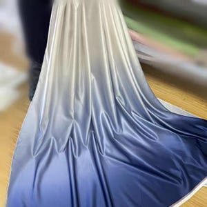 May include: A length of fabric with a colour gradient, fading from white to deep blue. The material has a shiny finish, with folds and drapes visible. Suitable for clothing or interior design projects.