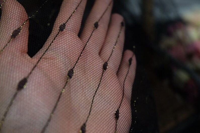 May include: Black sheer fabric with gold glitter dots and lines. The fabric is delicate and has a soft, flowing texture.