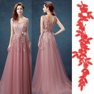 Könnte beinhalten: Ein staubiges rosafarbenes Tüllkleid mit zarten Blumenstickereien und einer passenden Schleife. Das Kleid hat einen V-Ausschnitt und ist ärmellos.