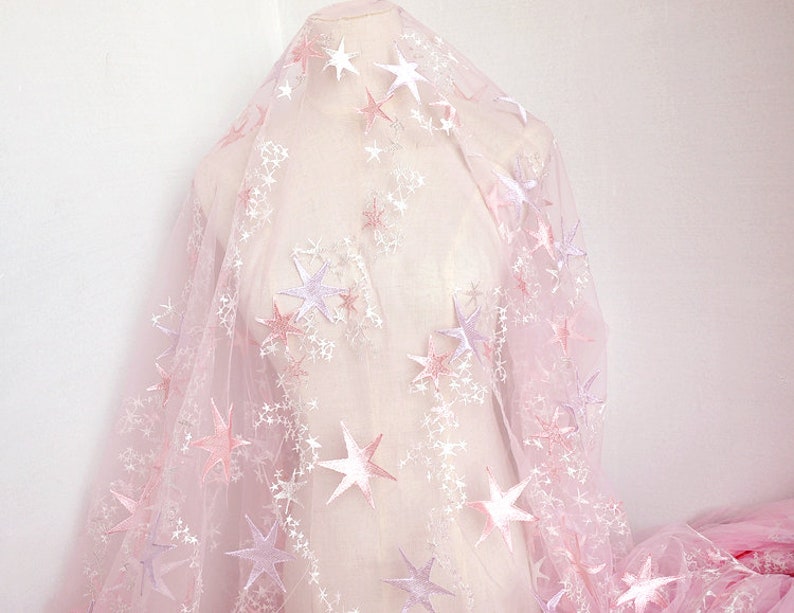 May include: Pink tulle fabric with embroidered white and pink stars. The fabric is sheer and delicate, perfect for crafting or adding a touch of whimsy to a project.