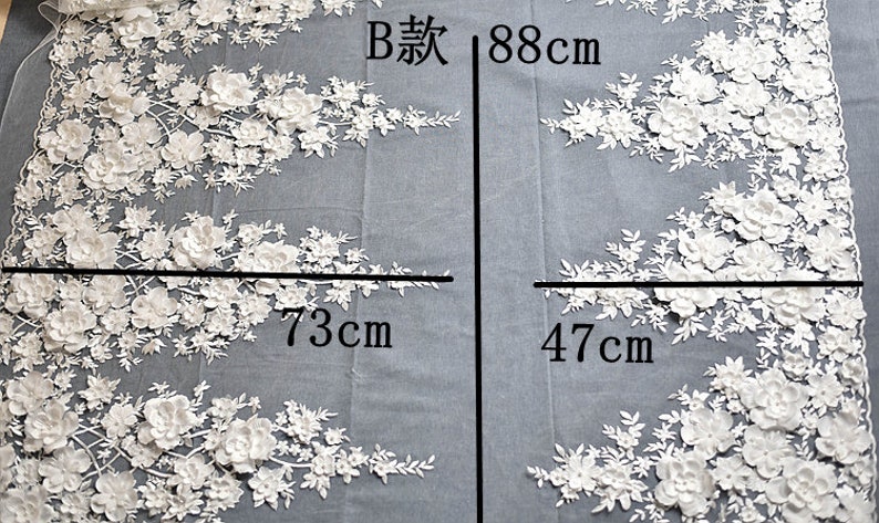 May include: White floral lace fabric with a 3D effect. The fabric is 73cm wide and 88cm long. The fabric is on a gray background. The text 'B款 88cm' is written on the fabric.