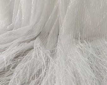 Puede incluir: Tela de tul blanco con una delicada franja y un brillo sutil. La tela es transparente y ligera, lo que la hace ideal para crear una variedad de prendas y accesorios.