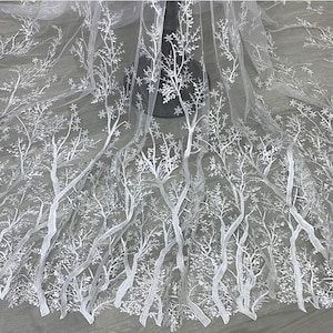 Peut inclure: Un tissu blanc transparent orné d'une broderie blanche complexe représentant des branches d'arbres dénudées et un feuillage délicat. La broderie crée un motif dense et répétitif de troncs verticaux et de branches s'étendant sur le matériau.