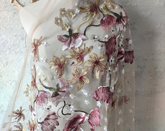 Op de afbeelding: Beige tule stof met geborduurde bloemenmotieven in roze, goud en groene tinten.