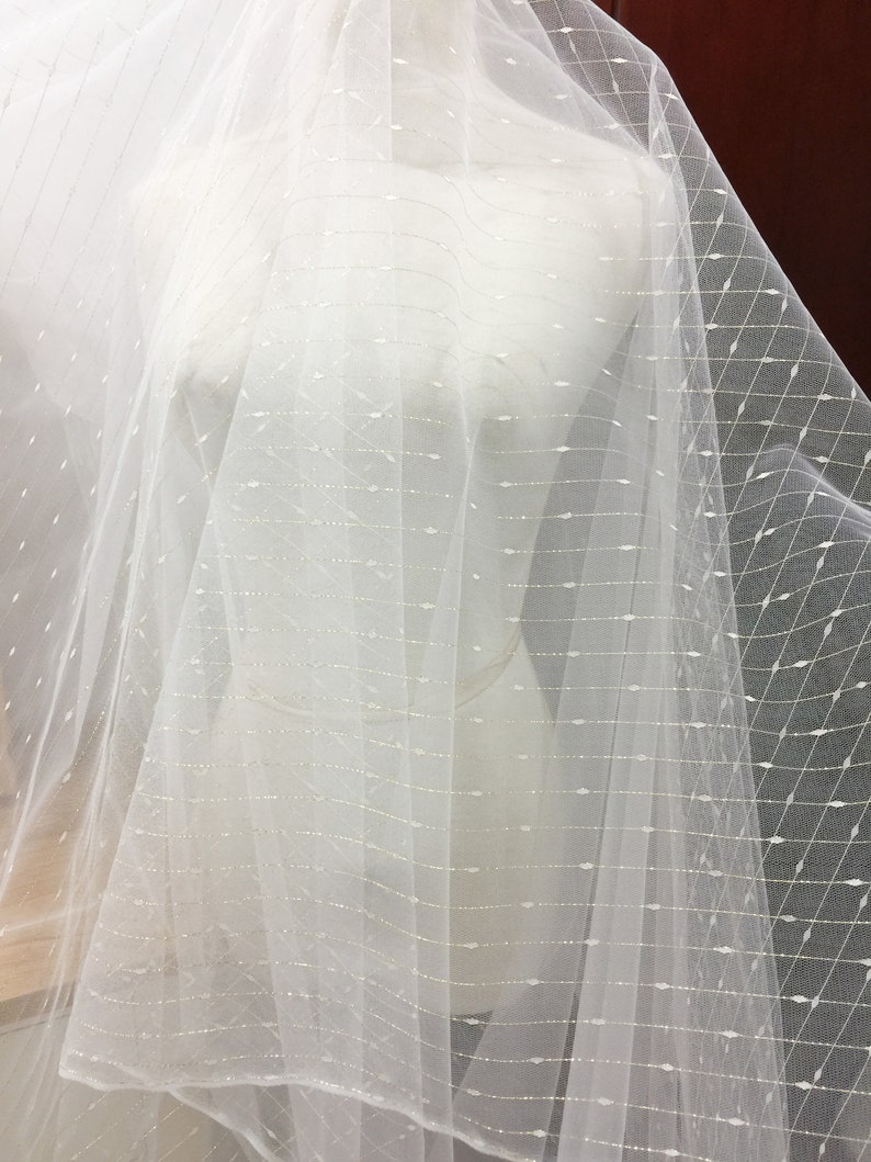 May include: White tulle fabric with a delicate pattern of silver thread. The fabric is sheer and has a soft, flowing texture.