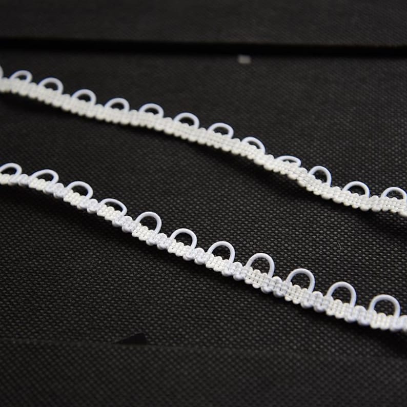 May include: White elastic trim with a scalloped edge. The trim has a series of small loops along the edge.