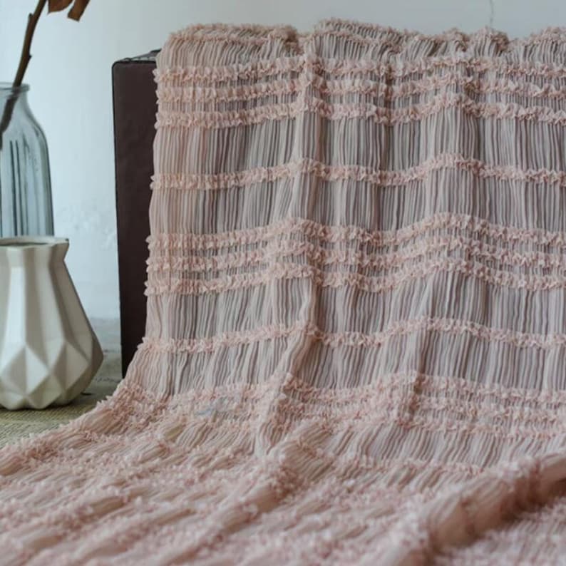 May include: A pale pink fabric with a textured, crinkled, and ruffled design. The fabric has a delicate, airy feel and is perfect for creating garments, home decor, or accessories.