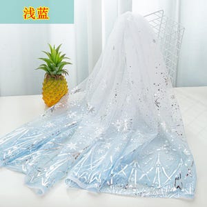 May include: A sheer white and light blue fabric with silver snowflake and geometric patterns. The fabric has a gradient effect, transitioning from white to light blue. The Chinese text "浅蓝" is visible in the upper left corner.