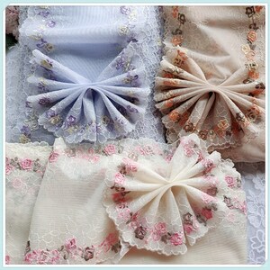 May include: Three pieces of delicate, embroidered fabric with floral patterns. Each piece is folded into a bow shape, showcasing the intricate lace details. The fabrics are in shades of light blue, peach, and cream.